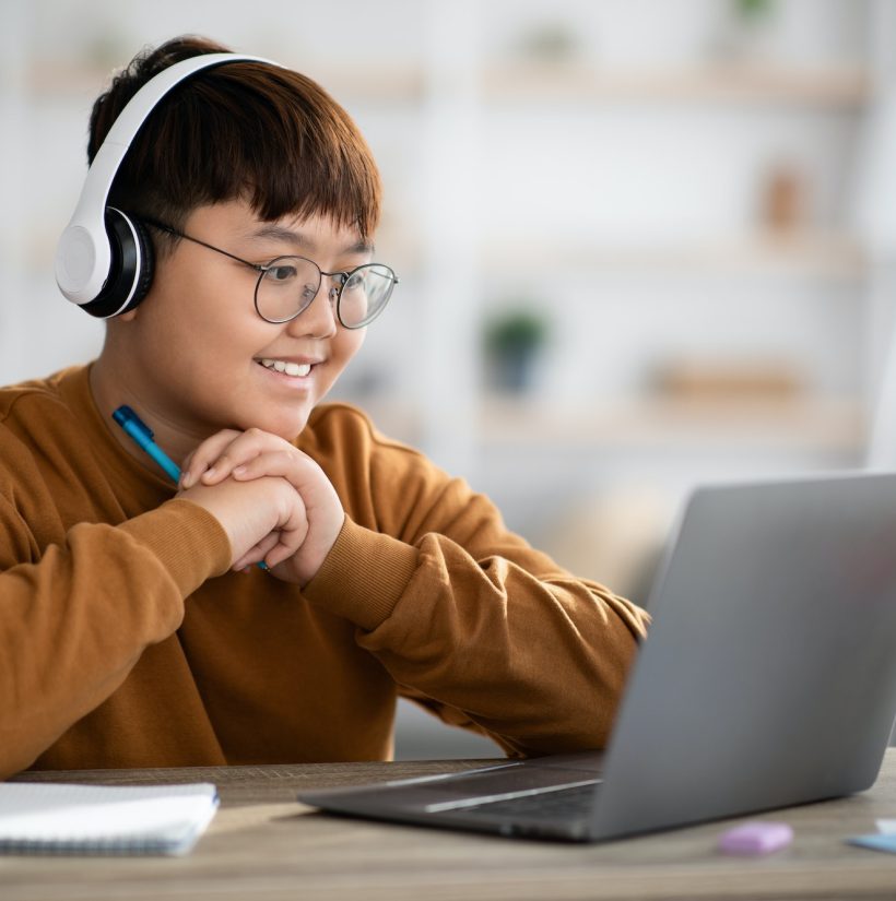 Cheerful asian boy schooler having online lesson from home