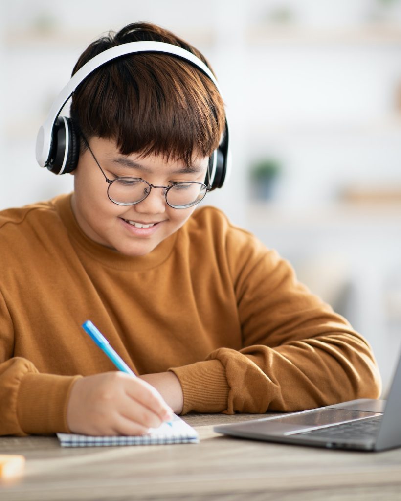 Smiling asian boy schooler having online lesson from home